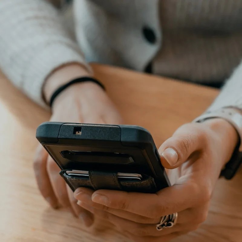 Person sitting at a desk and using a black mobile phone